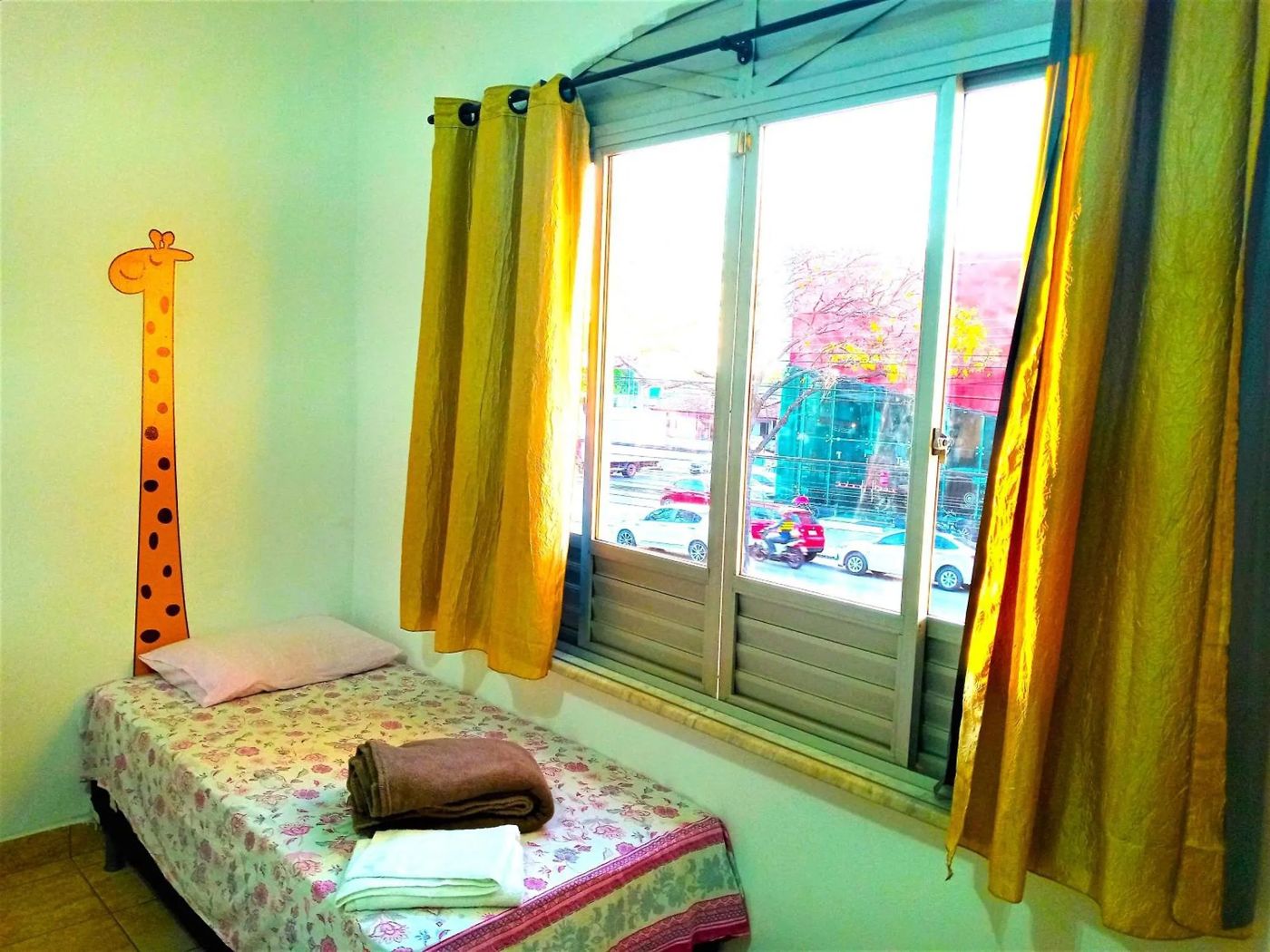 Quarto triplo com cama junto à janela e cortinas coloridas